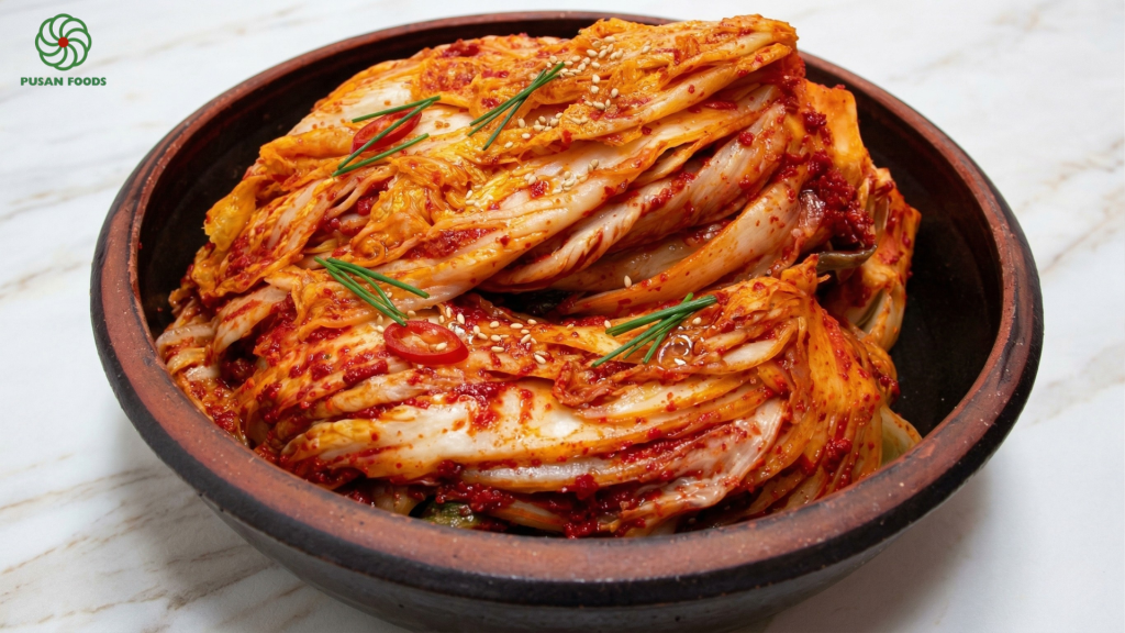 Một đĩa kim chi cải thảo đỏ au, óng ả, có rắc chút mè trắng lên trên. Hình ảnh phải cho thấy được độ giòn của bẹ cải và độ sánh của sốt. Nên đặt trong bối cảnh bàn gỗ ấm cúng.