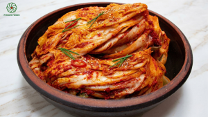 Một đĩa kim chi cải thảo đỏ au, óng ả, có rắc chút mè trắng lên trên. Hình ảnh phải cho thấy được độ giòn của bẹ cải và độ sánh của sốt. Nên đặt trong bối cảnh bàn gỗ ấm cúng.