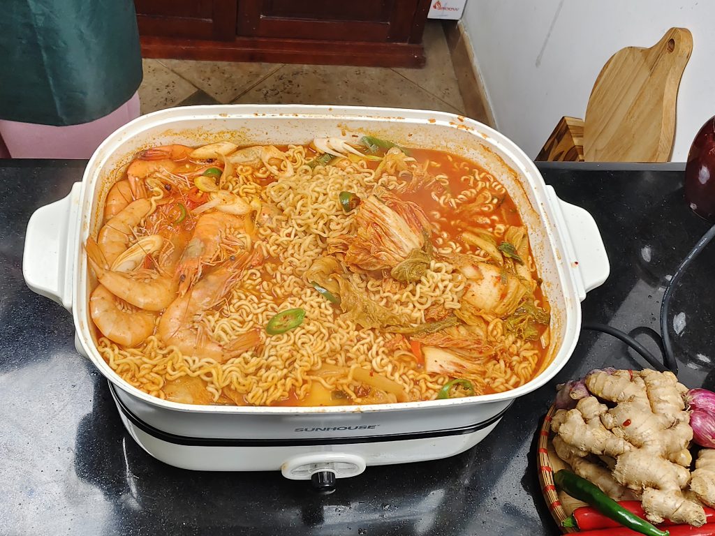 Một nồi canh kim chi (Kimchi Jjigae) đang sôi sùng sục với đậu phụ và thịt ba chỉ. Màu nước dùng đỏ cam đậm đà, hấp dẫn.