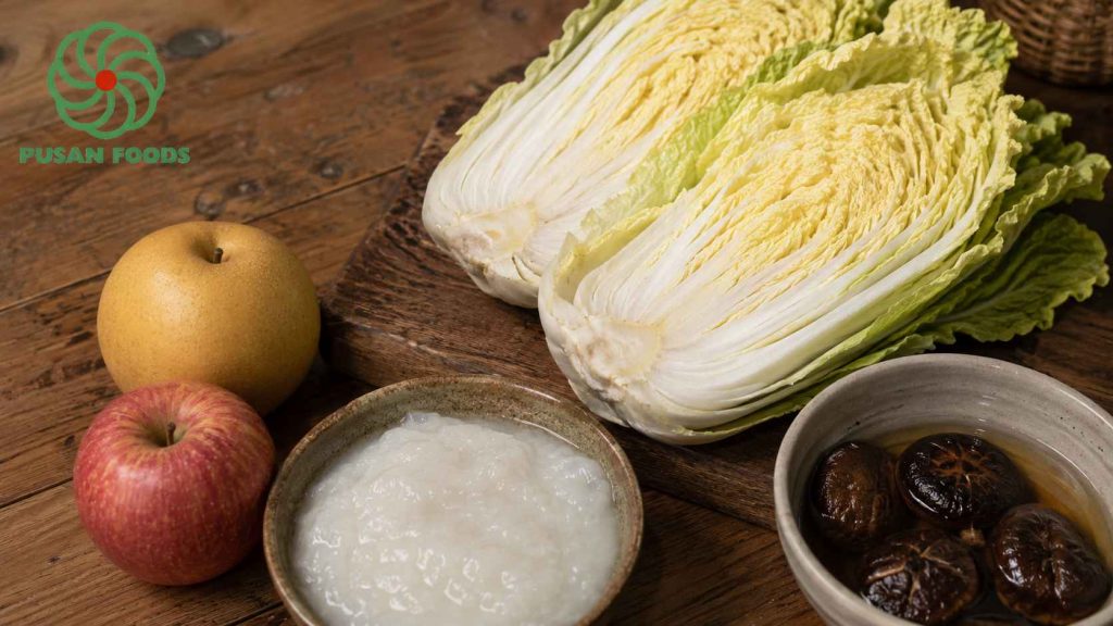 Sắp xếp các nguyên liệu chính trên mặt bàn gỗ: Bắp cải thảo bổ đôi, quả lê, quả táo, nấm hương khô đang ngâm, và bát bột nếp quấy sẵn. Cách sắp xếp hơi ngẫu hứng, tạo cảm giác bếp núc thực tế chứ không phải ảnh studio cứng nhắc.